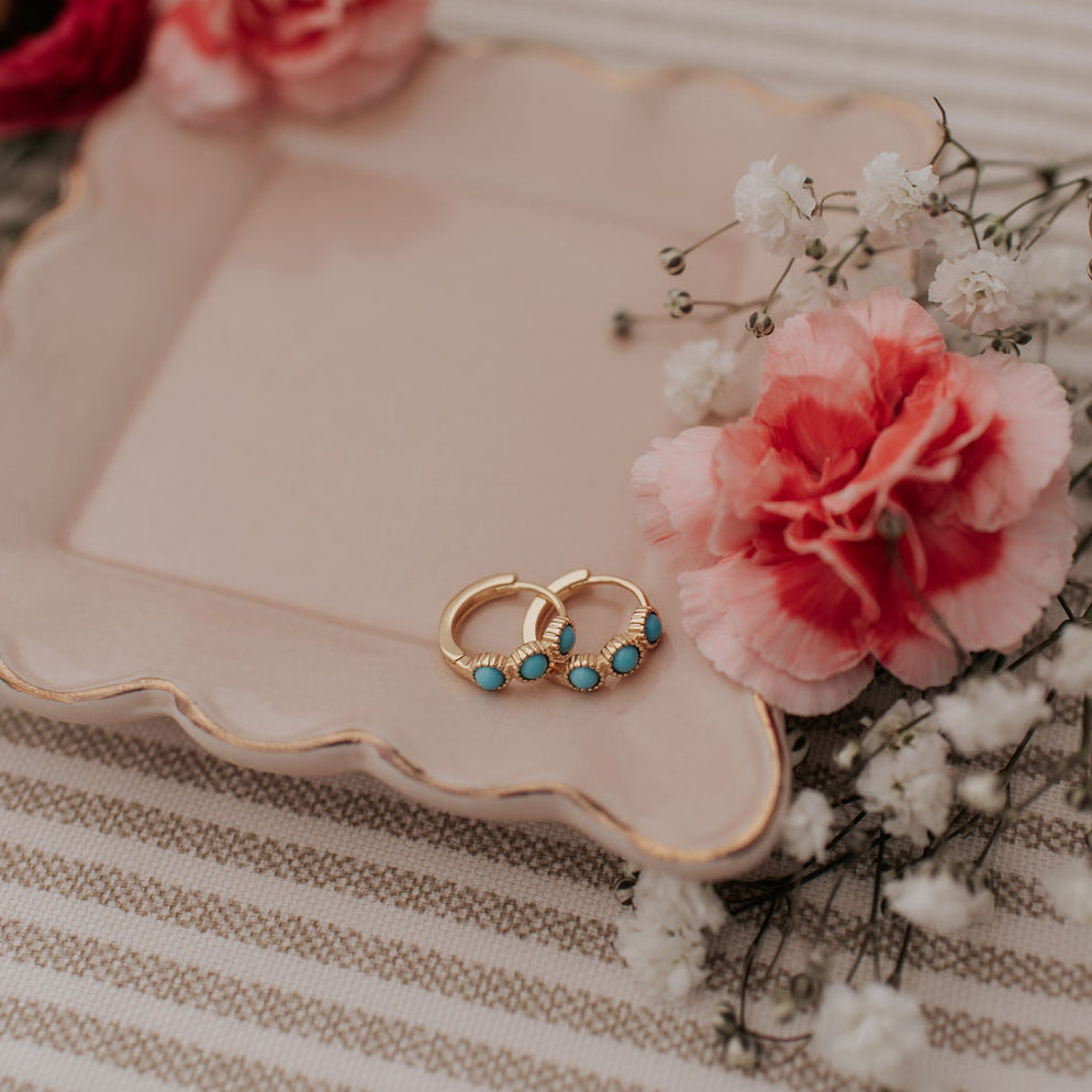 Gold turquoise huggie hoops shown together on a tray.