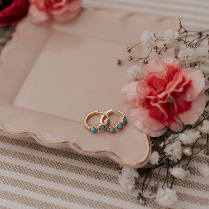 Gold turquoise huggie hoops shown together on a tray.