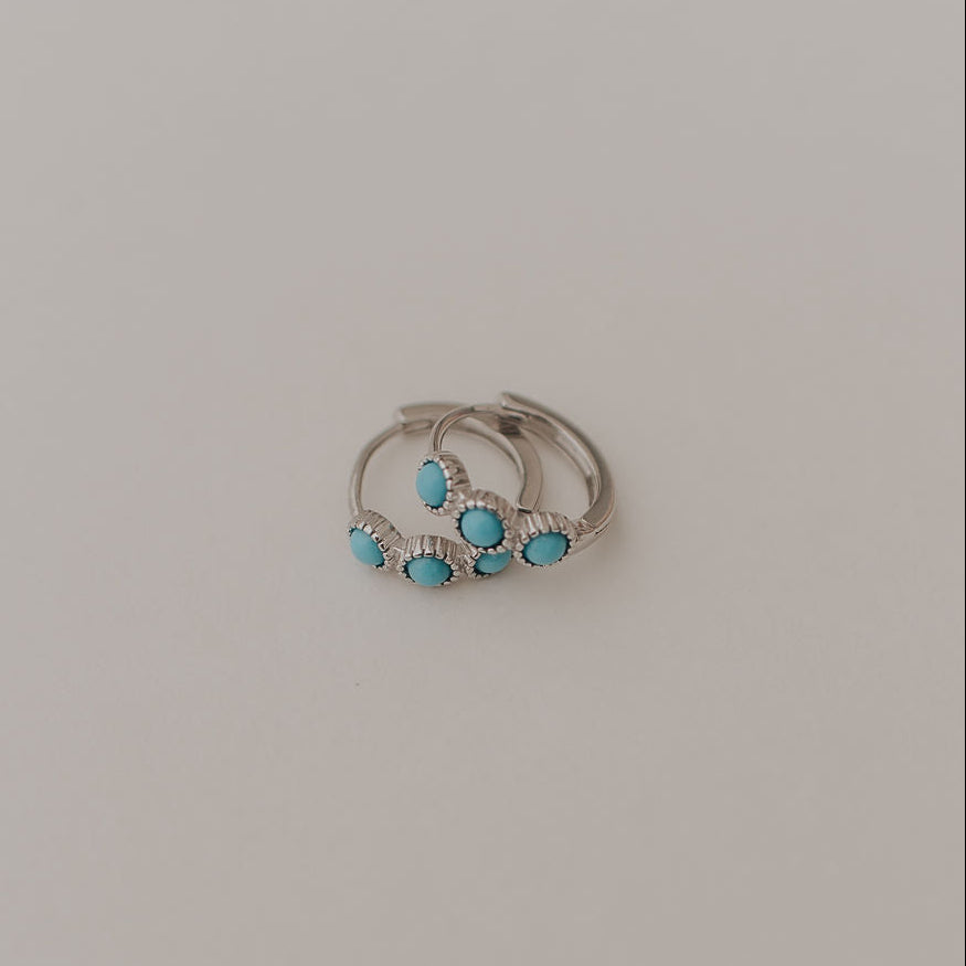 Silver turquoise huggie hoop earrings shown together from the front.