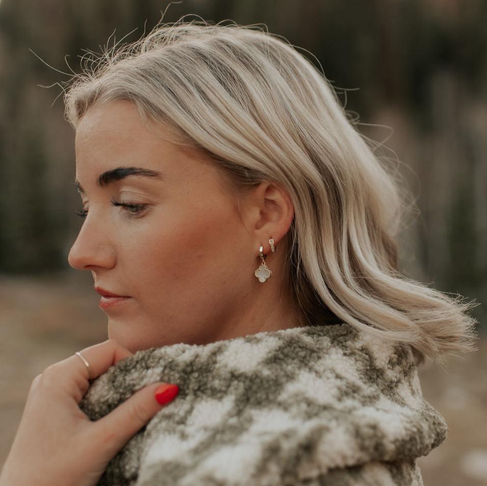 Gold huggie hoop with a mother-of-pearl clover charm, worn on the ear
