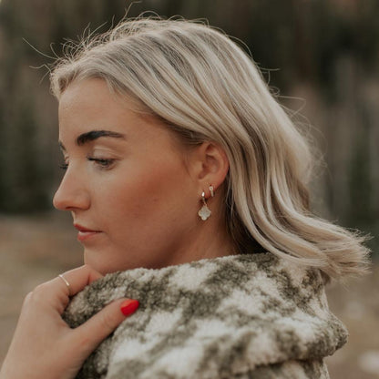 Gold huggie hoop with a mother-of-pearl clover charm, worn on the ear