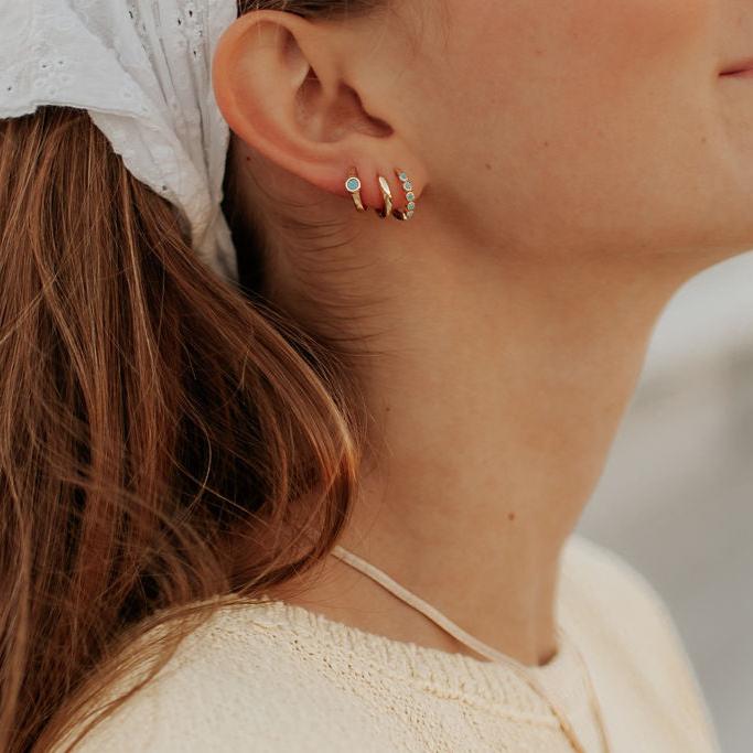 Small gold-tone hoops with turquoise accents worn in multiple piercings