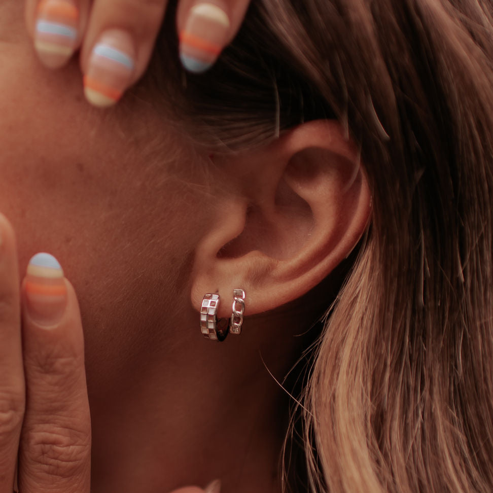 Pair of brown and white checkered silver hoops worn on an ear