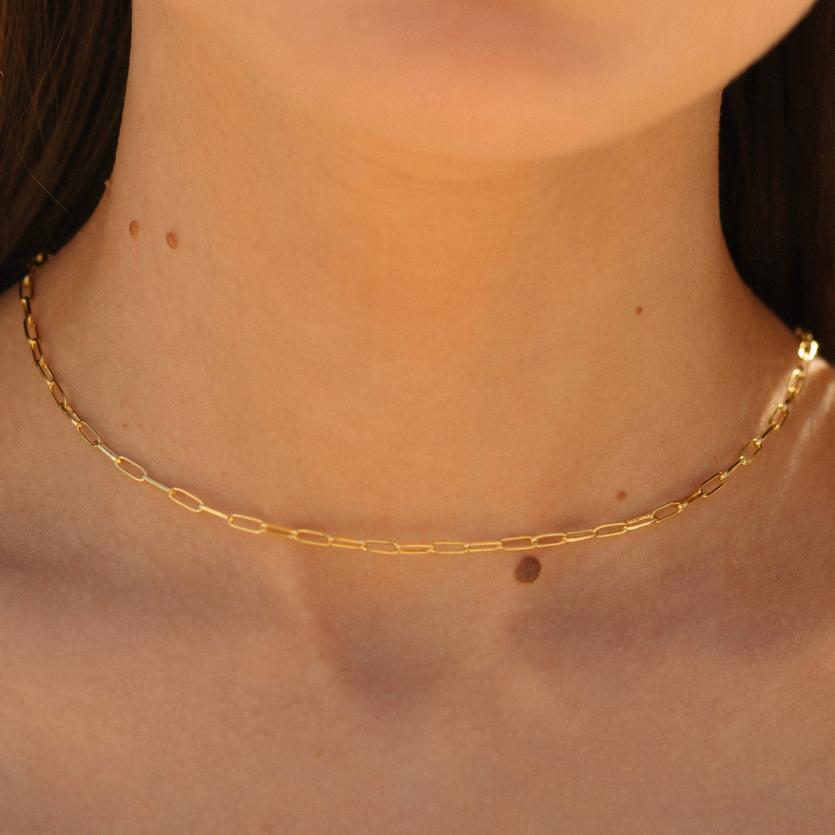 Gold paperclip chain necklace with oval links, close-up at collarbone