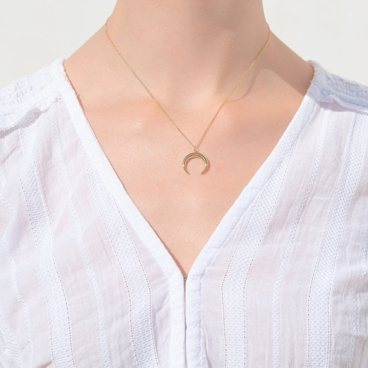 Gold crescent moon pendant necklace worn on a V-neckline