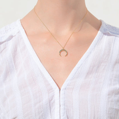 Gold crescent moon pendant necklace worn on a V-neckline