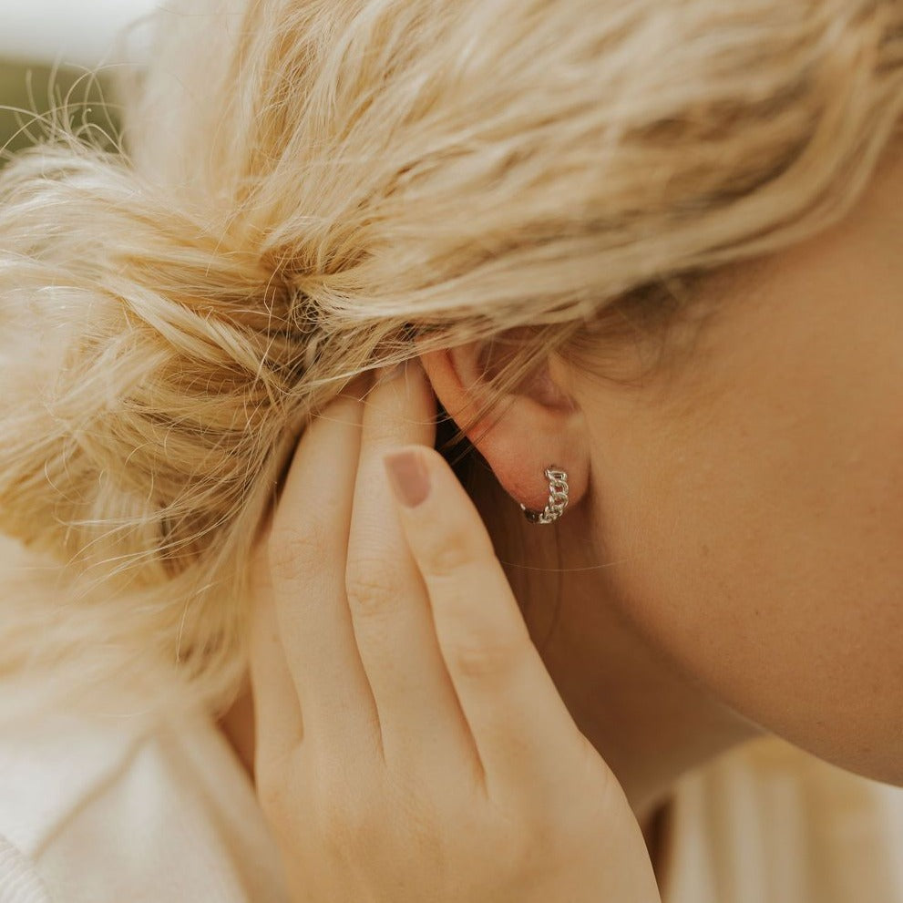 Gold Peri hoop earring worn close-up, showing its textured links.