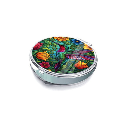 Silver compact mirror shown closed at an angle, with a hummingbird and floral cover