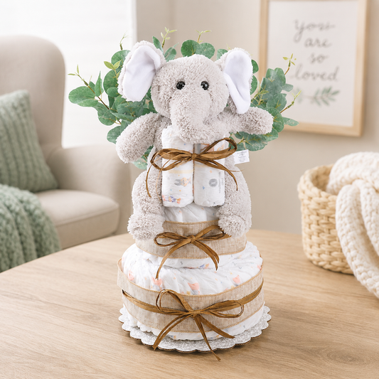 Two-tier baby diaper cake gift with plush elephant, diaper layers, leaf accents, ribbon ties