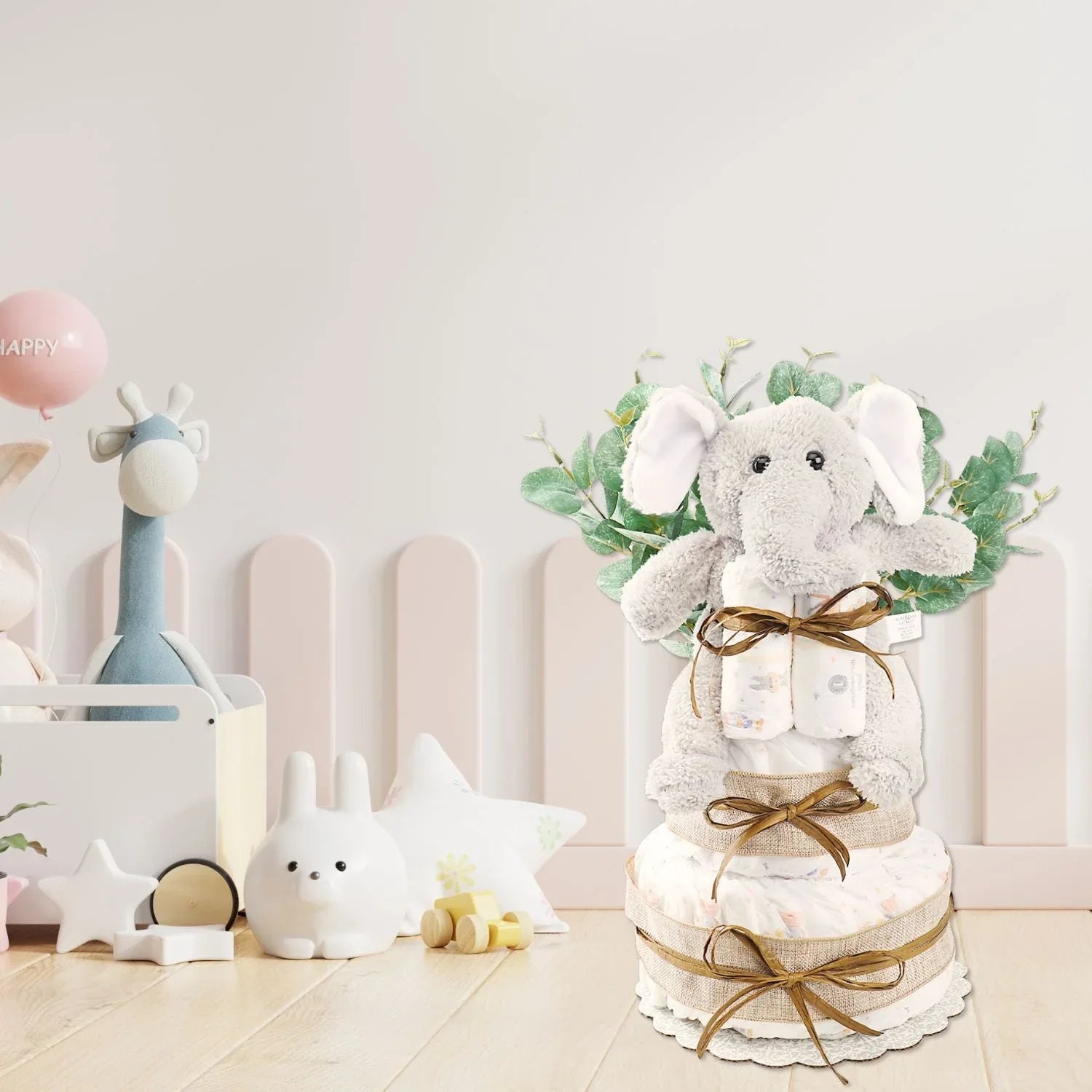 Two-tier diaper cake gift with plush elephant topper, mint-green leaf accents, gold ribbon ties