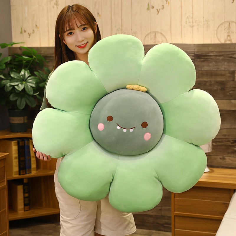 Mint-green plush flower pillow with round gray face, smiling details, and pink blush cheeks
