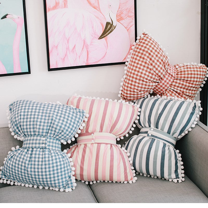Bow-shaped decorative pillows in blue gingham, pink stripes, and blue-and-white stripes
