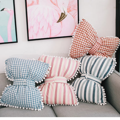 Bow-shaped decorative pillows in blue gingham, pink stripes, and blue-and-white stripes