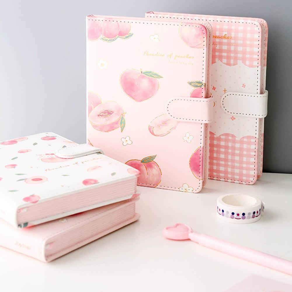 Pink notebook with peach illustrations, stitched bands, and a wide strap closure across front
