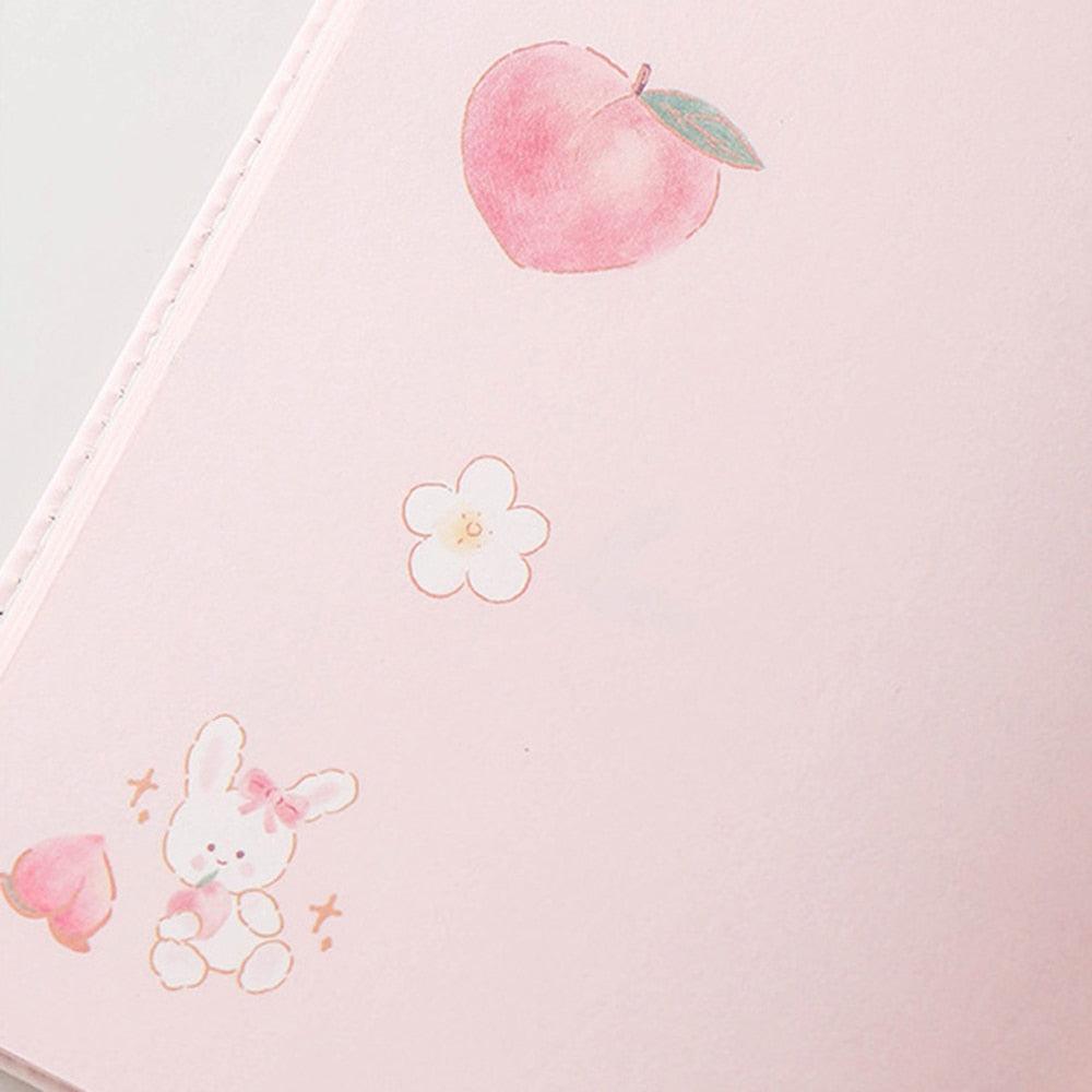Pink notebook cover close-up with peach and flower line icons and small dotted accents