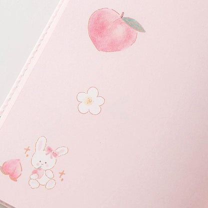 Pink notebook cover close-up with peach and flower line icons and small dotted accents