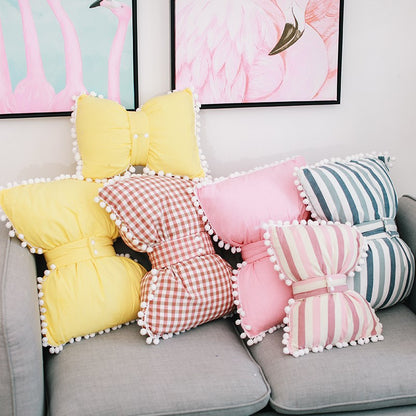 Assorted bow-shaped decorative pillows in yellow, red gingham, pink, and blue stripes