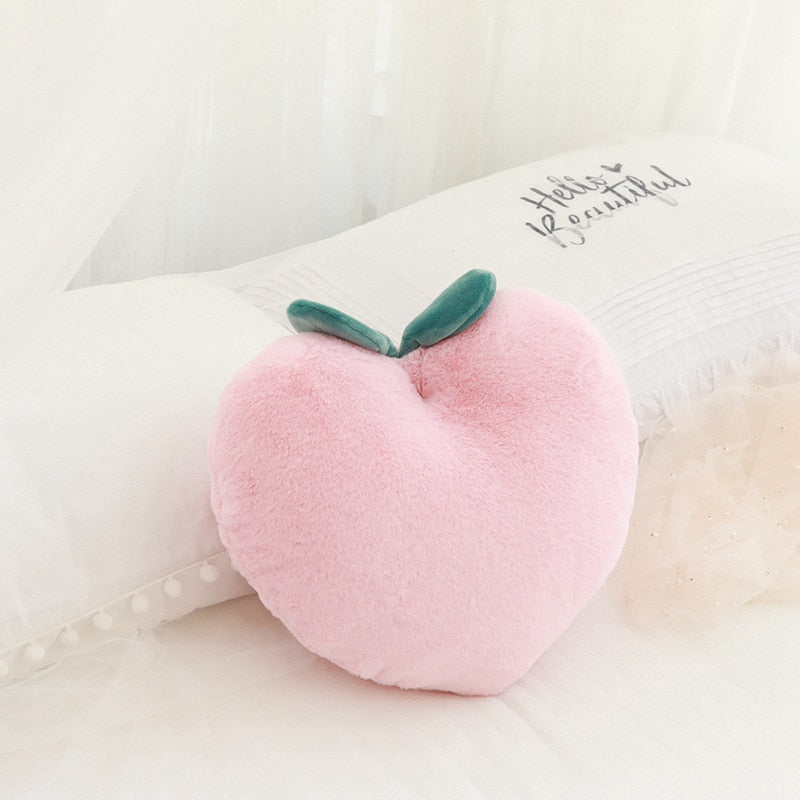 Pink plush peach pillow with green leaves, lying on a soft bed