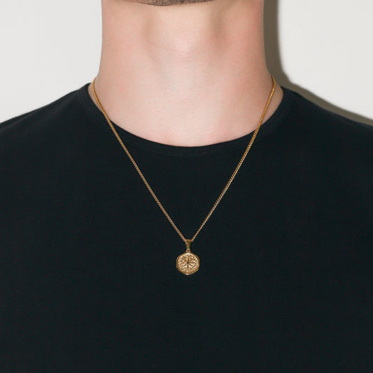 Gold chain necklace with small round compass pendant on a neckline