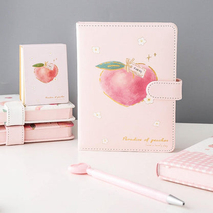 Pink peach notebook with strap and stitched design, featuring a large peach graphic on the cover