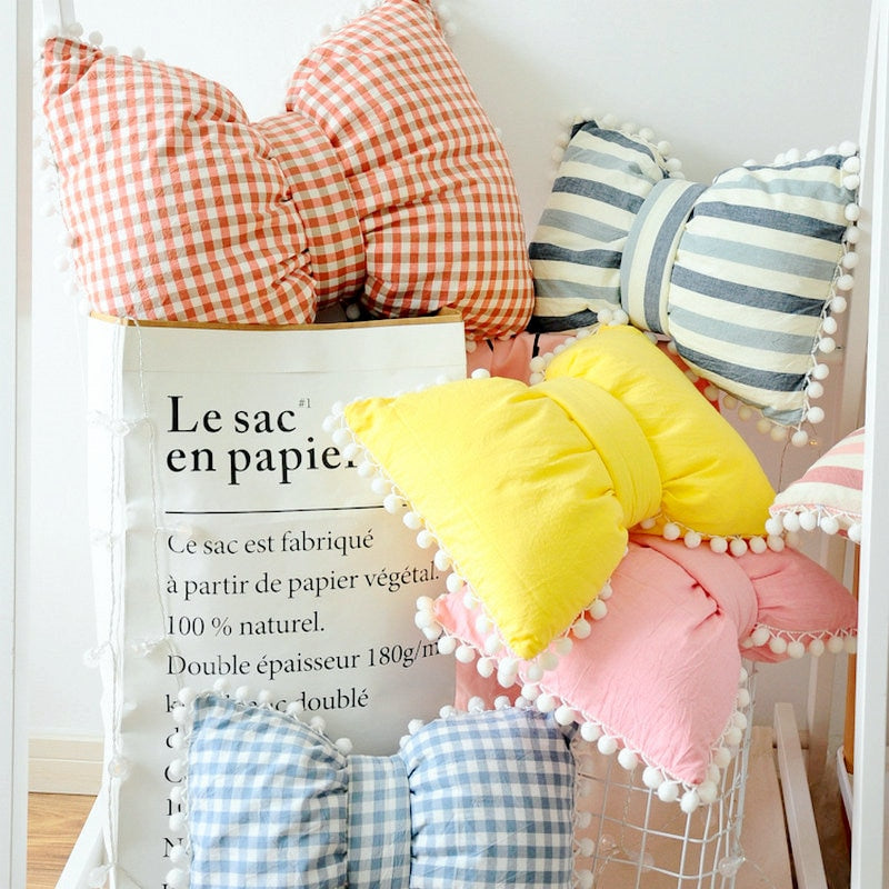 Multicolor bow-shaped decorative pillows: orange gingham, blue stripes, yellow, pom trim