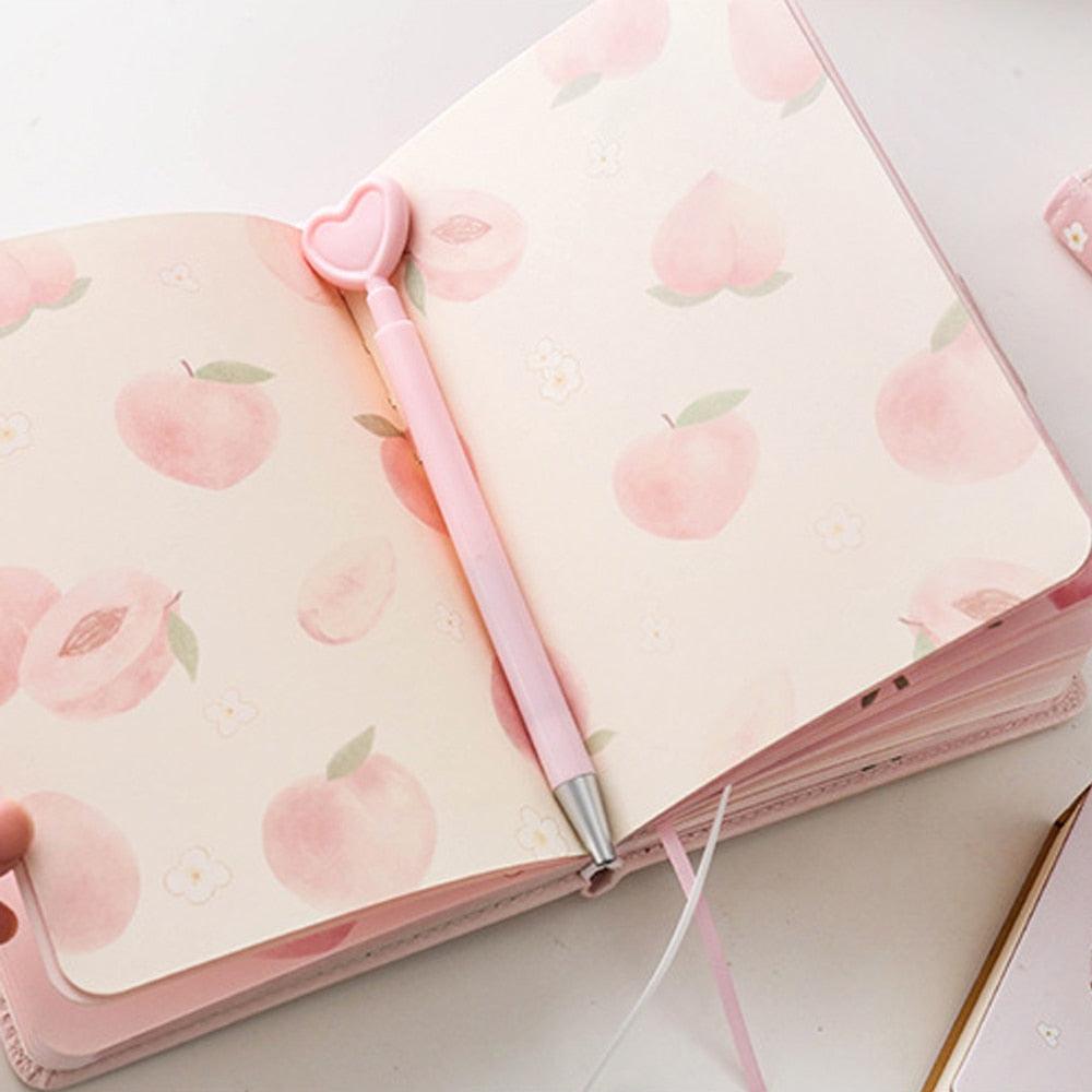 Pink notebook open to peach-pattern pages, with a pink pen and heart-shaped cap