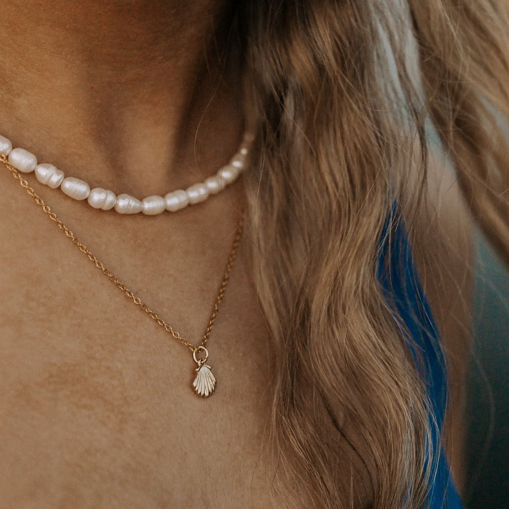 Gold shell pendant necklace worn below a strand of white pearls