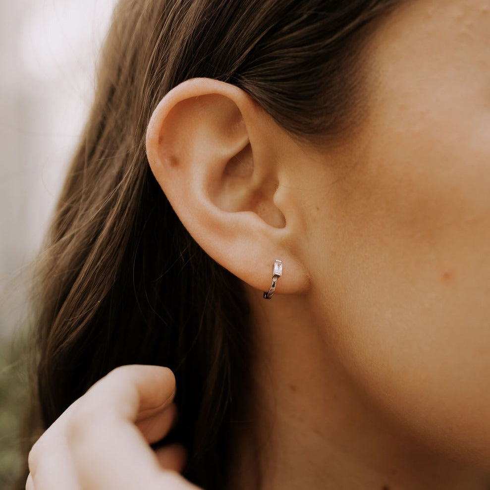 Silver baguette diamond mini hoop earring worn in the ear