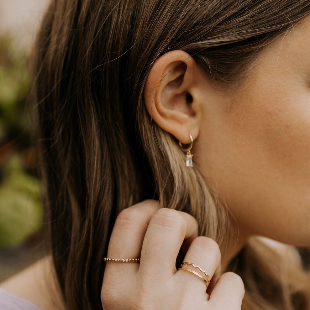 Gold dangle hoop with a clear baguette-cut stone, worn on the ear