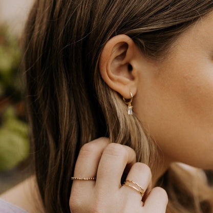 Gold dangle hoop with a clear baguette-cut stone, worn on the ear