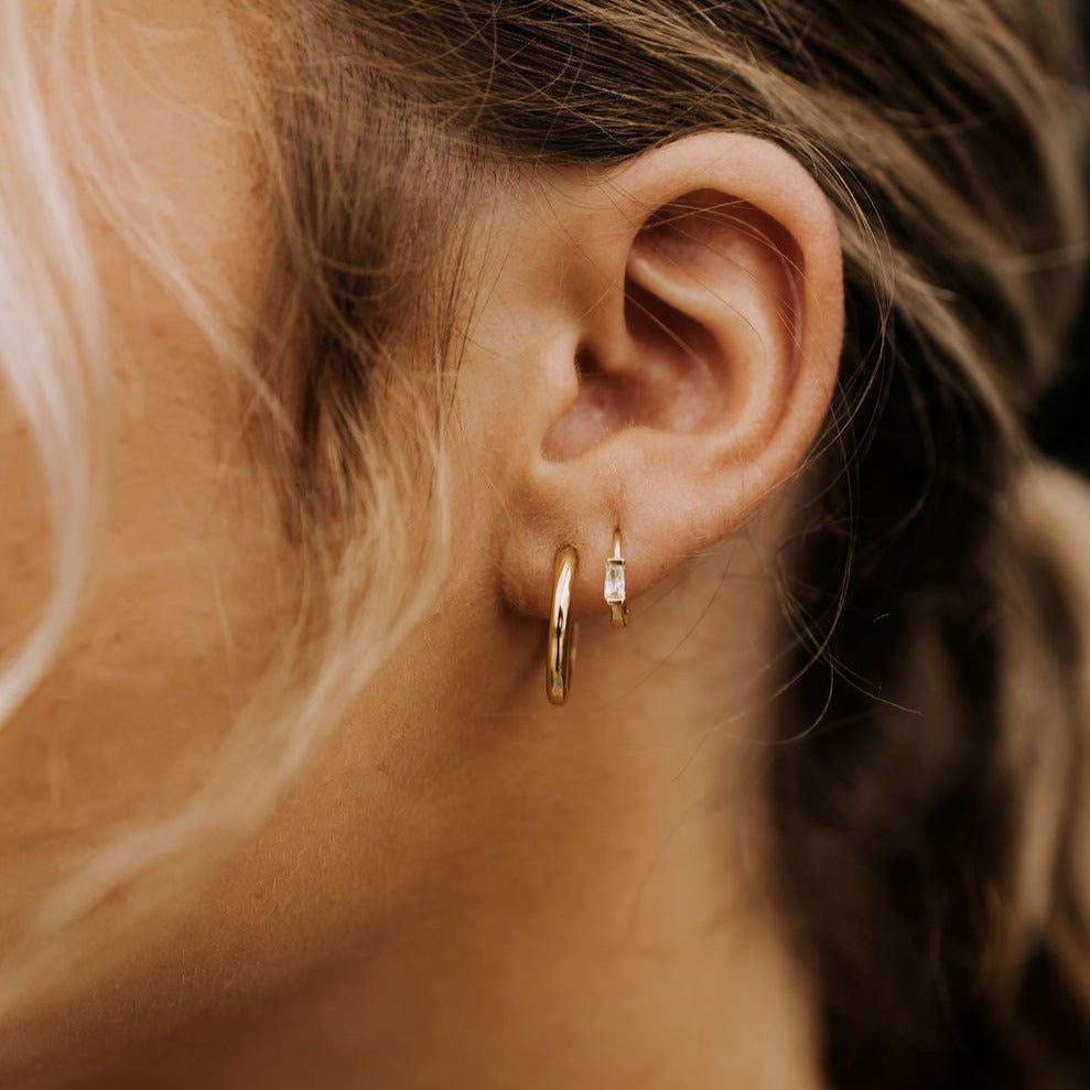 Gold baguette diamond mini hoop earring worn beside a larger hoop