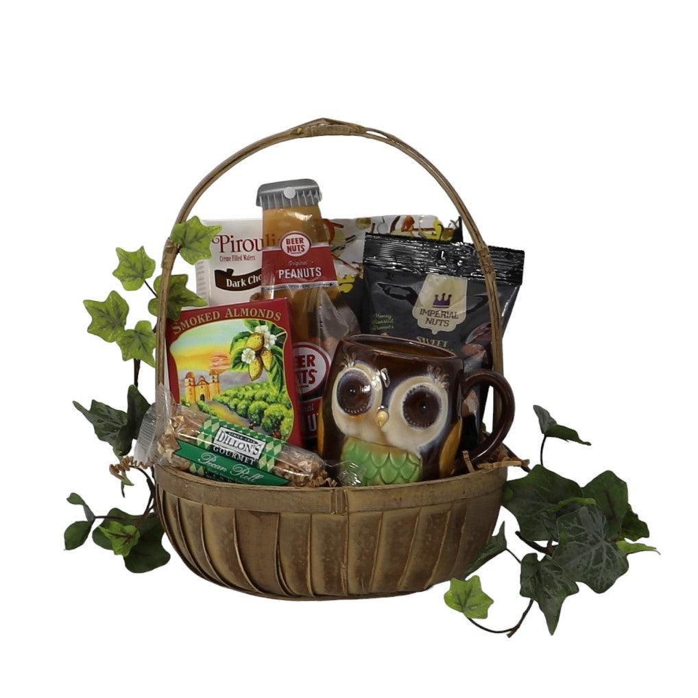 Wicker gift basket filled with gourmet snacks, nuts, chocolate, and an owl mug.