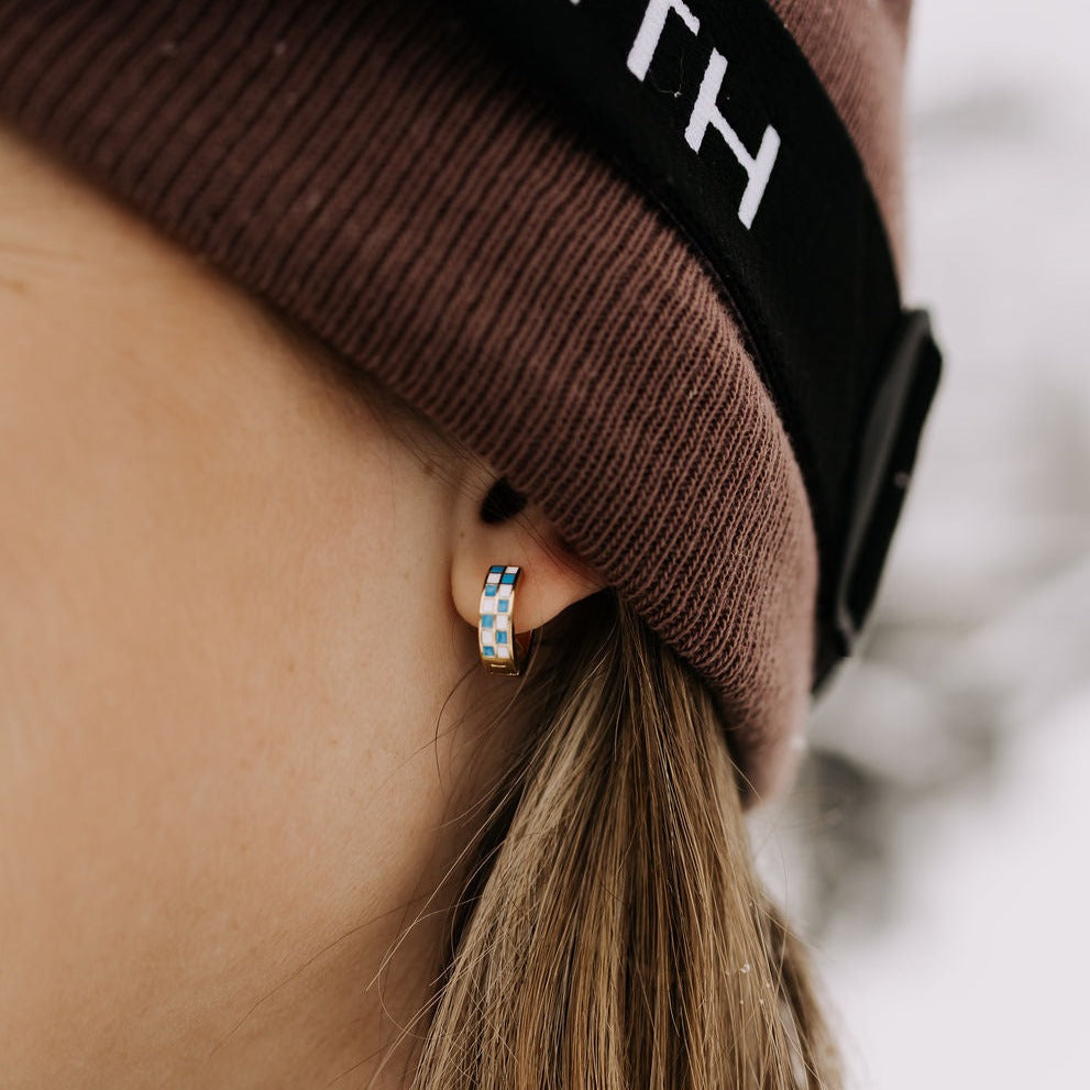 Blue and white checkered gold-tone hoop earring worn on an ear