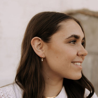 Gold dangle hoop with a clear stone, shown worn from the side