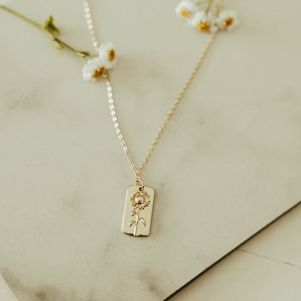 Gold chain necklace with a rectangular sunflower pendant shown flat