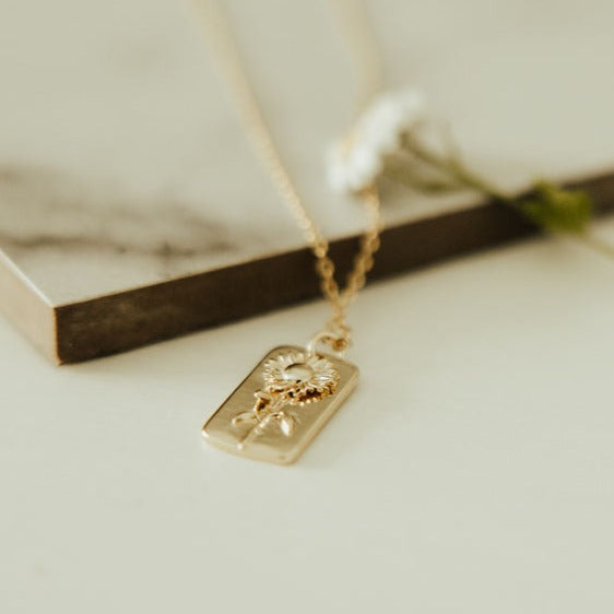 Low-angle close-up of a gold necklace's raised sunflower tag pendant
