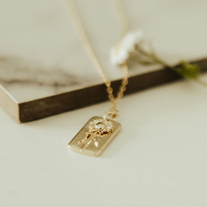 Low-angle close-up of a gold necklace's raised sunflower tag pendant