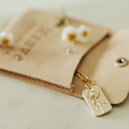 Gold sunflower pendant necklace with a rectangular tag and delicate chain