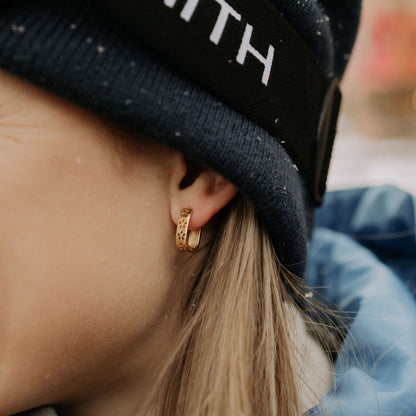 Gold reversible hoop earring worn on an ear, showing its floral-patterned side