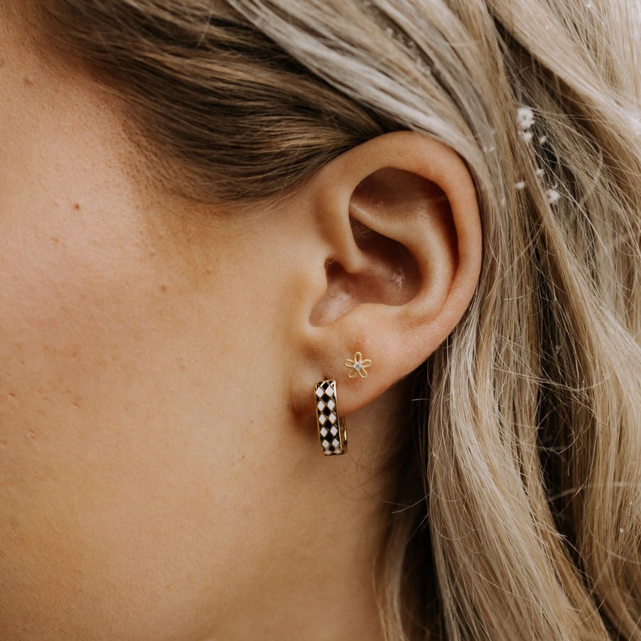 Gold hoop earring worn on an ear, showing its black-and-white diamond pattern