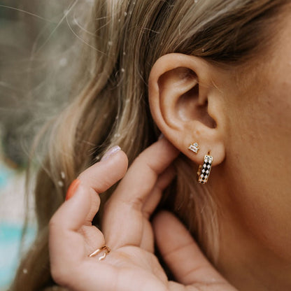 Black-and-white diamond-patterned gold hoop earring worn on an ear