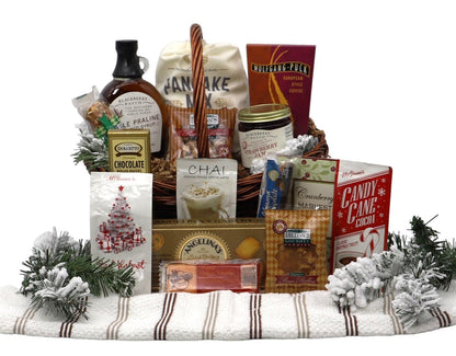 Large gift basket on striped blanket with holiday treats and pine greenery.