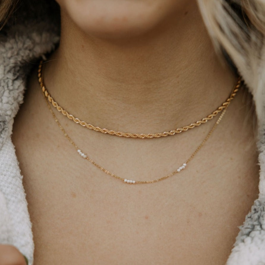 Delicate gold-tone chain necklace with spaced white pearl accents, layered below a thicker chain