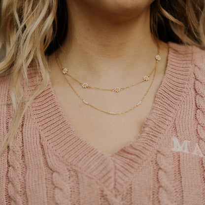 Fine gold-tone pearl necklace layered beneath a daisy-accented necklace