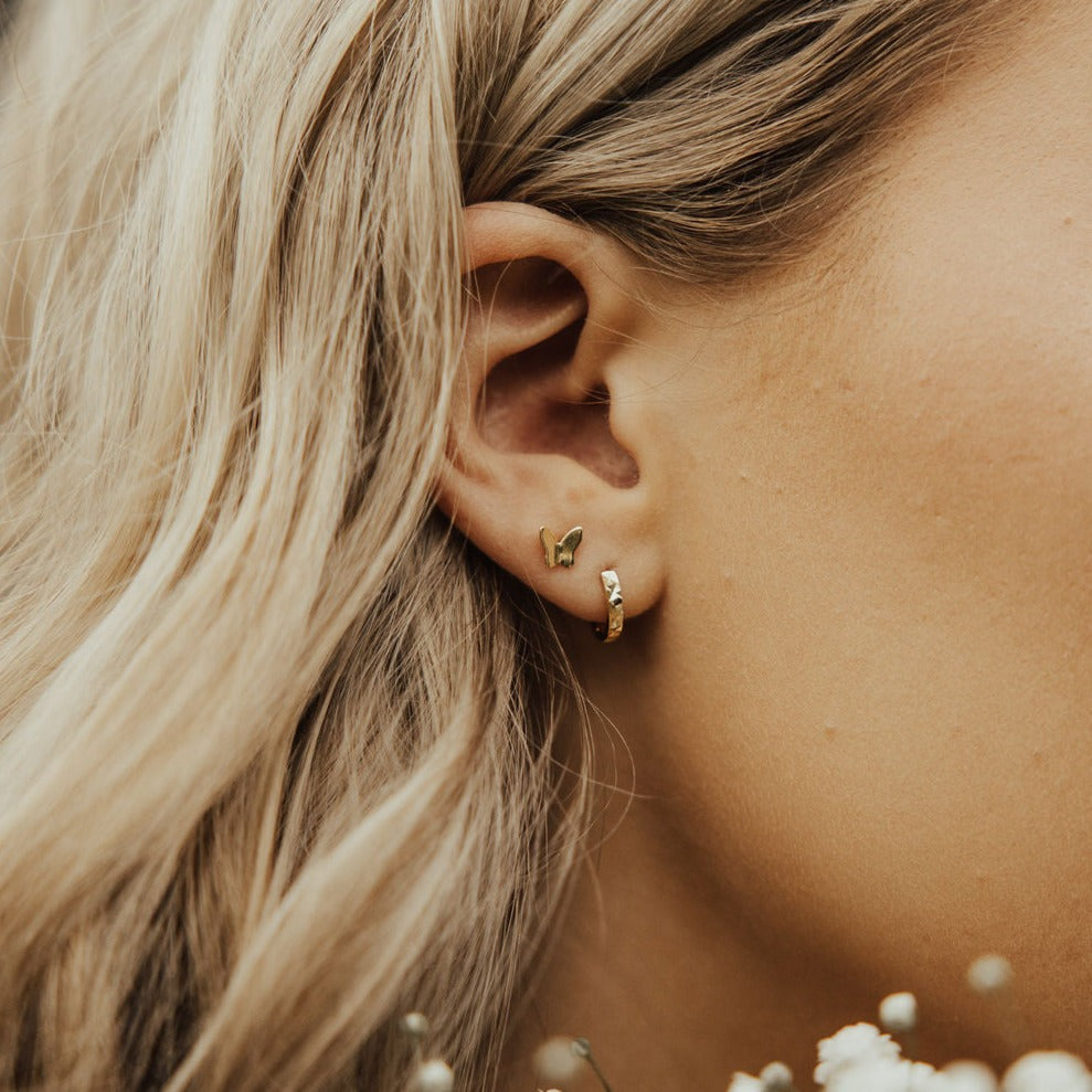 Gold butterfly mini stud worn above a small hoop earring