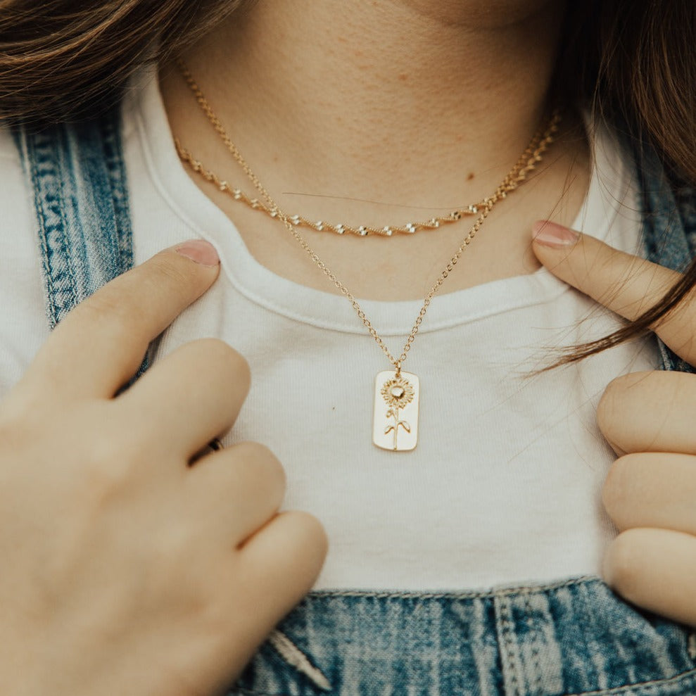 Gold necklace with a sunflower tag pendant, shown worn at the chest