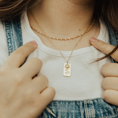 Gold necklace with a sunflower tag pendant, shown worn at the chest