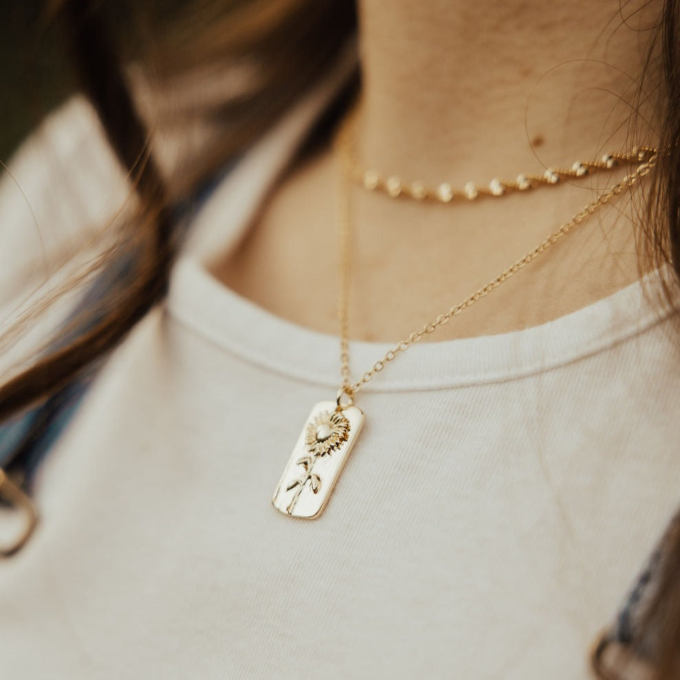 Close view of a gold sunflower pendant necklace worn on a fine chain