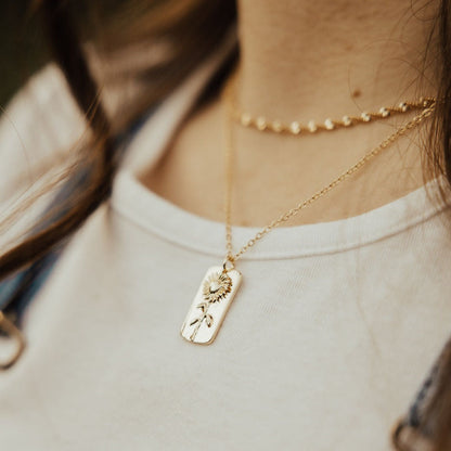 Close view of a gold sunflower pendant necklace worn on a fine chain