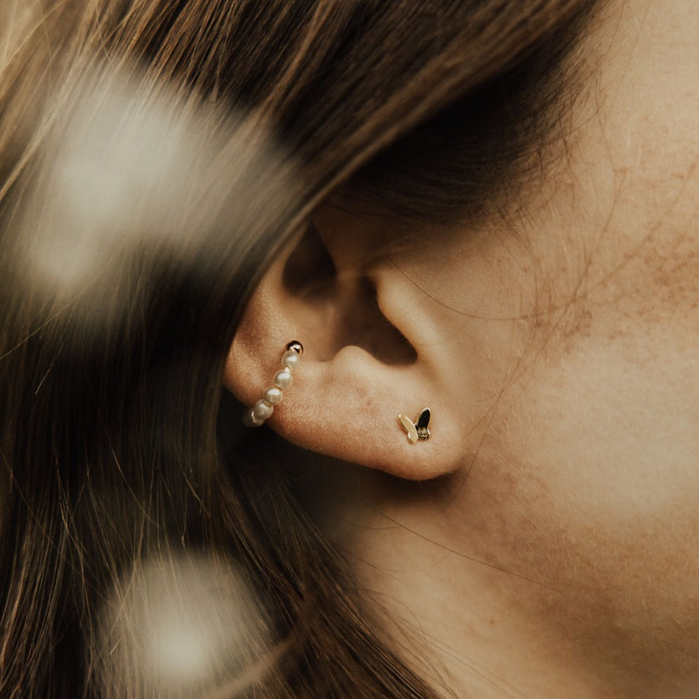 Gold butterfly mini stud worn in an ear, shown in close-up